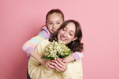 Photo of Girl giving her mother beautiful bouquet of lily-of-the-valley flowers on light pink background