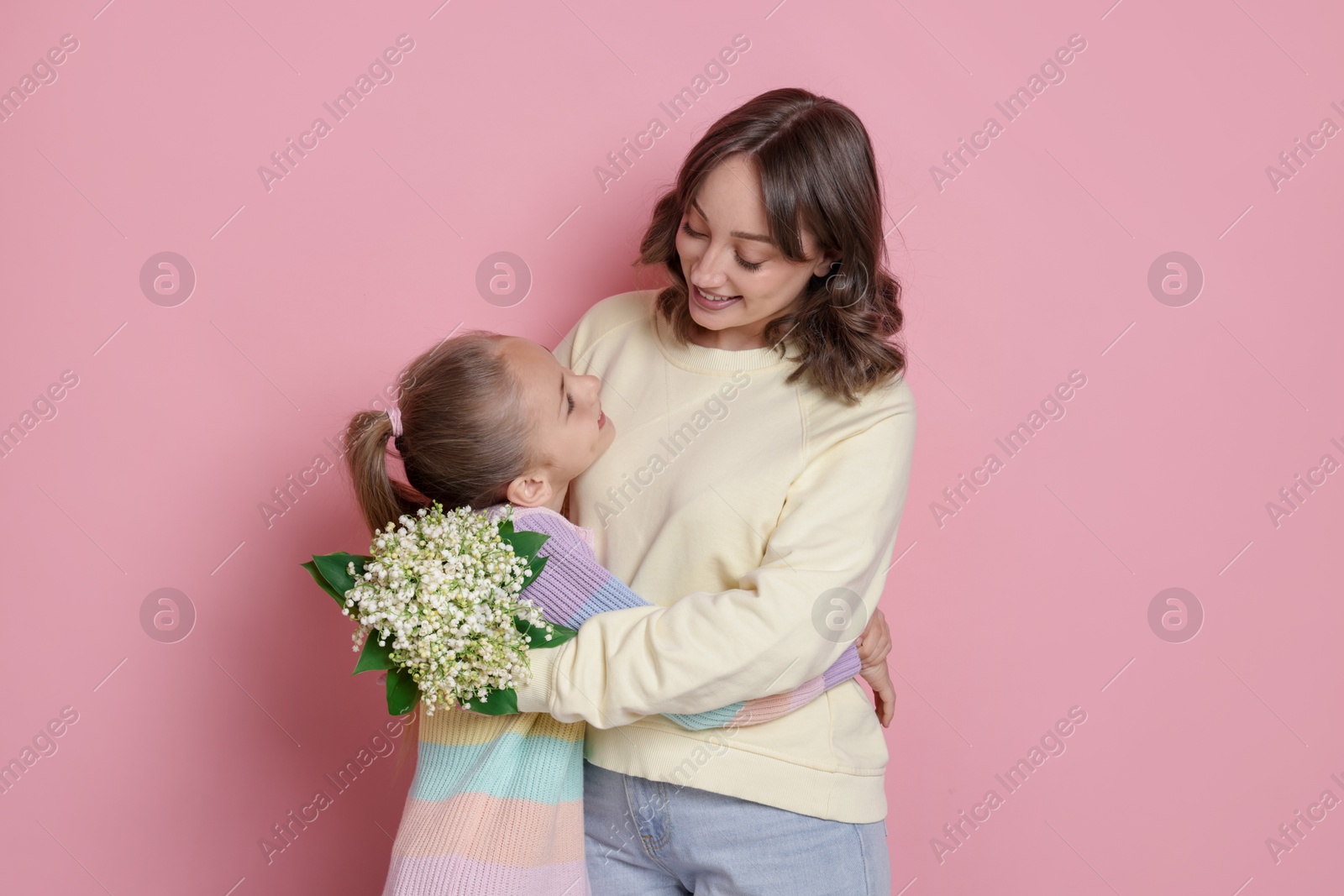 Girl giving her mother beautiful bouquet of lily-of-the-valley flowers on light pink background Photo of Girl giving her mother beautiful bouquet of lily-of-the-valley flowers on light pink background