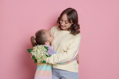 Photo of Girl giving her mother beautiful bouquet of lily-of-the-valley flowers on light pink background