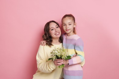Photo of Girl giving her mother beautiful bouquet of lily-of-the-valley flowers on light pink background