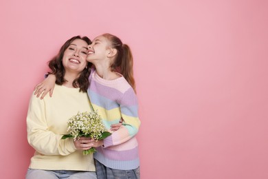 Photo of Girl giving her mother beautiful bouquet of lily-of-the-valley flowers on light pink background. Space for text