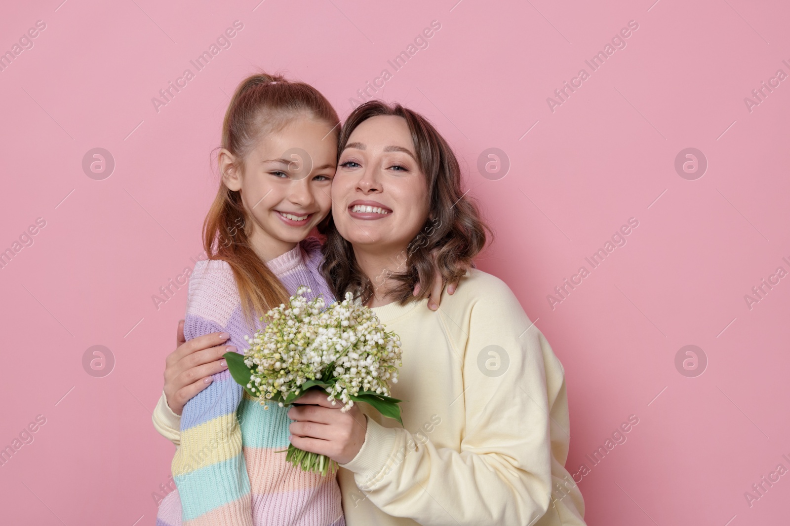 Girl giving her mother beautiful bouquet of lily-of-the-valley flowers on light pink background Photo of Girl giving her mother beautiful bouquet of lily-of-the-valley flowers on light pink background