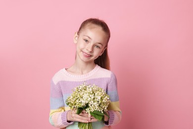 Photo of Girl with bouquet of beautiful lily-of-the-valley flowers on light pink background