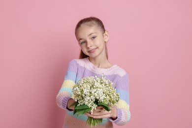 Photo of Girl with bouquet of beautiful lily-of-the-valley flowers on light pink background