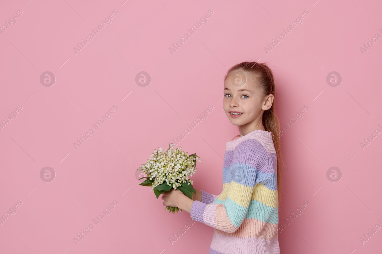 Girl with bouquet of beautiful lily-of-the-valley flowers on light pink background. Space for text Photo of Girl with bouquet of beautiful lily-of-the-valley flowers on light pink background. Space for text