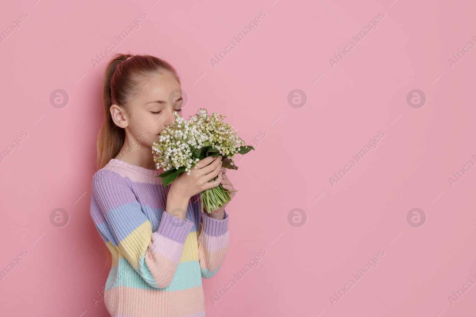 Girl with bouquet of beautiful lily-of-the-valley flowers on light pink background. Space for text Photo of Girl with bouquet of beautiful lily-of-the-valley flowers on light pink background. Space for text