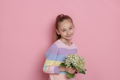 Photo of Girl with bouquet of beautiful lily-of-the-valley flowers on light pink background