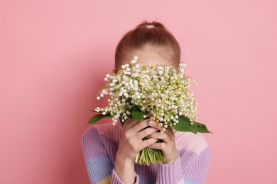 Photo of Girl with bouquet of beautiful lily-of-the-valley flowers on light pink background