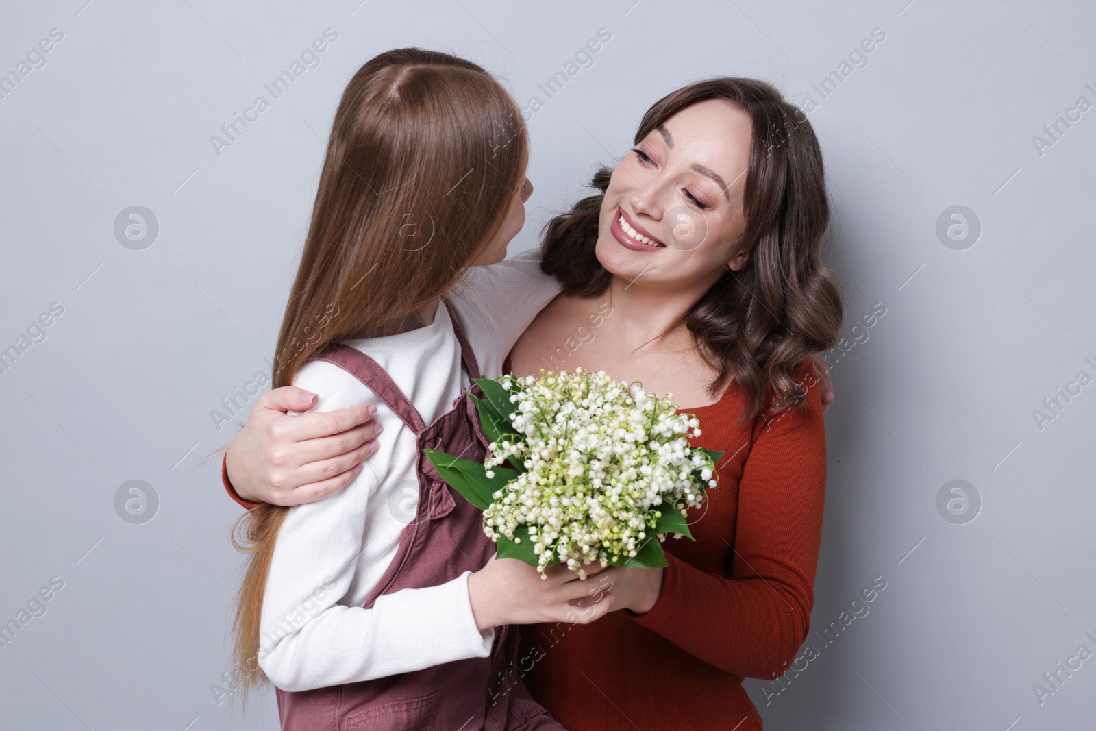 Girl giving her mom beautiful bouquet of lily-of-the-valley flowers on light grey background Photo of Girl giving her mom beautiful bouquet of lily-of-the-valley flowers on light grey background