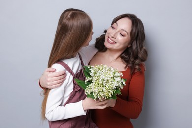Photo of Girl giving her mom beautiful bouquet of lily-of-the-valley flowers on light grey background