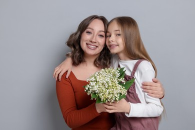 Photo of Girl giving her mom beautiful bouquet of lily-of-the-valley flowers on light grey background