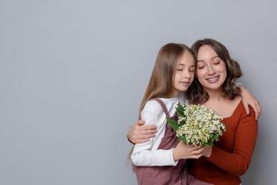 Photo of Girl giving her mom beautiful bouquet of lily-of-the-valley flowers on light grey background. Space for text