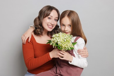 Photo of Girl giving her mom beautiful bouquet of lily-of-the-valley flowers on light grey background