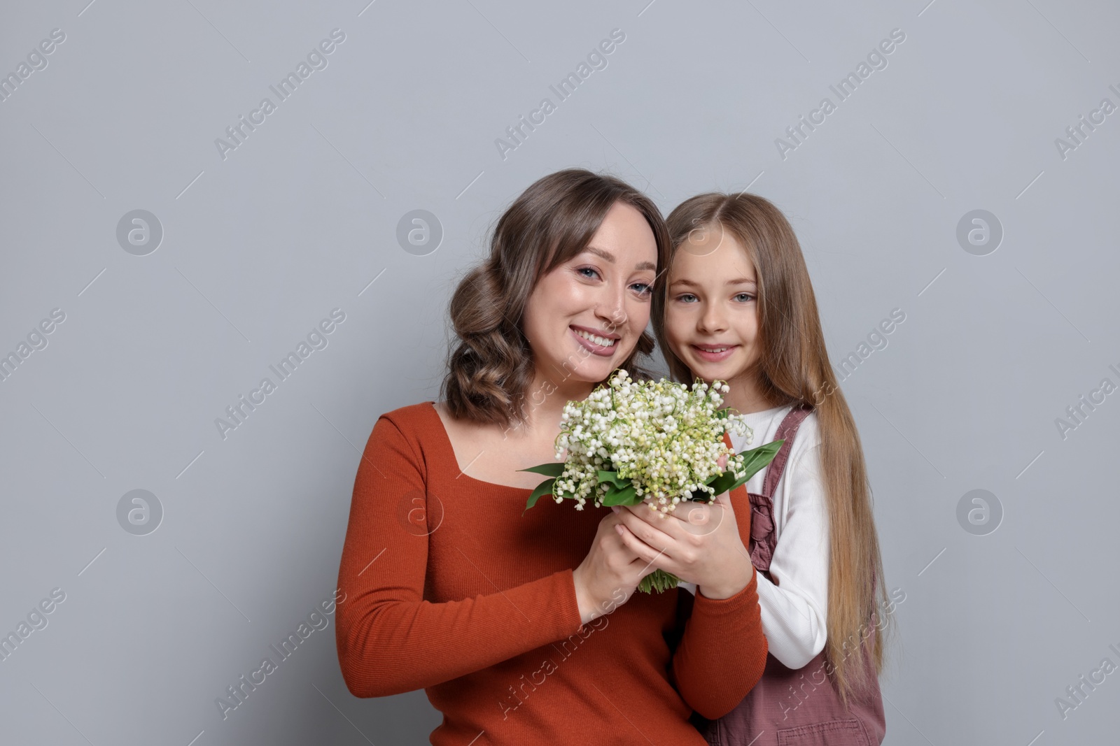 Girl giving her mom beautiful bouquet of lily-of-the-valley flowers on light grey background Photo of Girl giving her mom beautiful bouquet of lily-of-the-valley flowers on light grey background