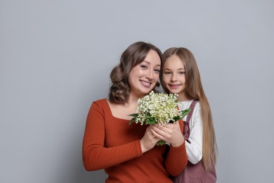 Photo of Girl giving her mom beautiful bouquet of lily-of-the-valley flowers on light grey background