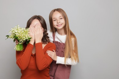 Photo of Girl giving her mom beautiful bouquet of lily-of-the-valley flowers on light grey background
