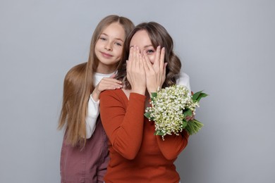Photo of Girl giving her mom beautiful bouquet of lily-of-the-valley flowers on light grey background