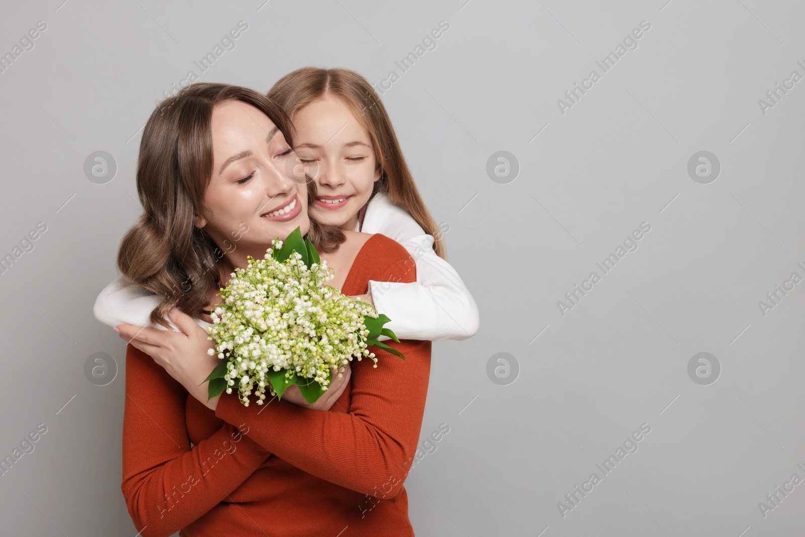 Girl giving her mom beautiful bouquet of lily-of-the-valley flowers on light grey background. Space for text Photo of Girl giving her mom beautiful bouquet of lily-of-the-valley flowers on light grey background. Space for text