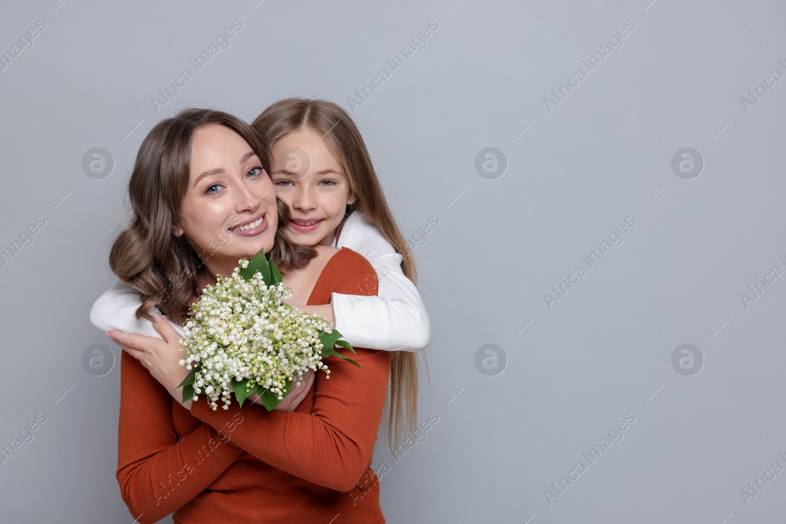 Girl giving her mom beautiful bouquet of lily-of-the-valley flowers on light grey background. Space for text Photo of Girl giving her mom beautiful bouquet of lily-of-the-valley flowers on light grey background. Space for text