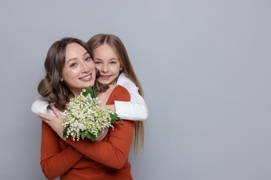 Photo of Girl giving her mom beautiful bouquet of lily-of-the-valley flowers on light grey background. Space for text