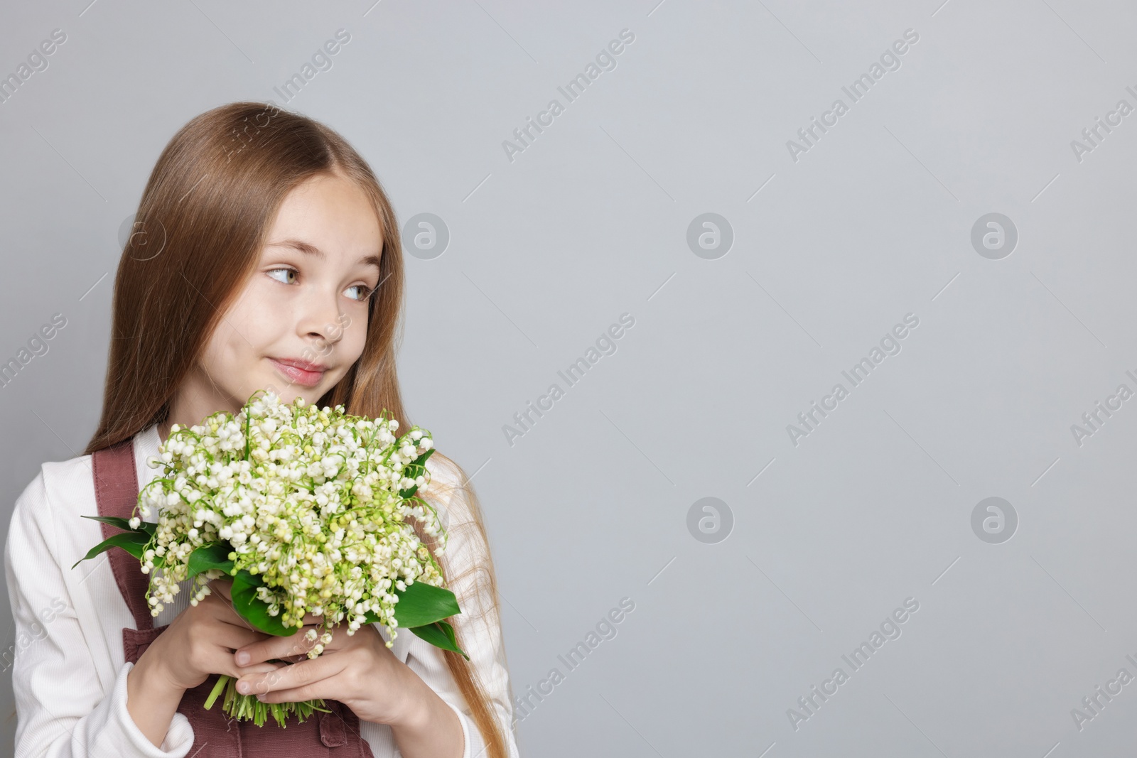 Girl with bouquet of beautiful lily-of-the-valley flowers on light grey background. Space for text Photo of Girl with bouquet of beautiful lily-of-the-valley flowers on light grey background. Space for text