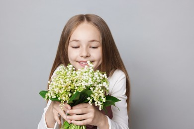 Photo of Girl with bouquet of beautiful lily-of-the-valley flowers on light grey background