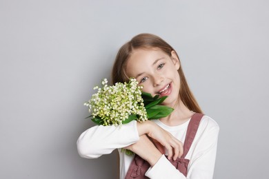 Photo of Girl with bouquet of beautiful lily-of-the-valley flowers on light grey background