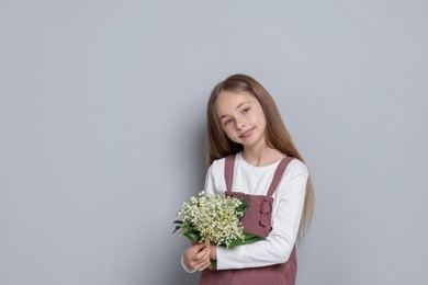 Photo of Girl with bouquet of beautiful lily-of-the-valley flowers on light grey background