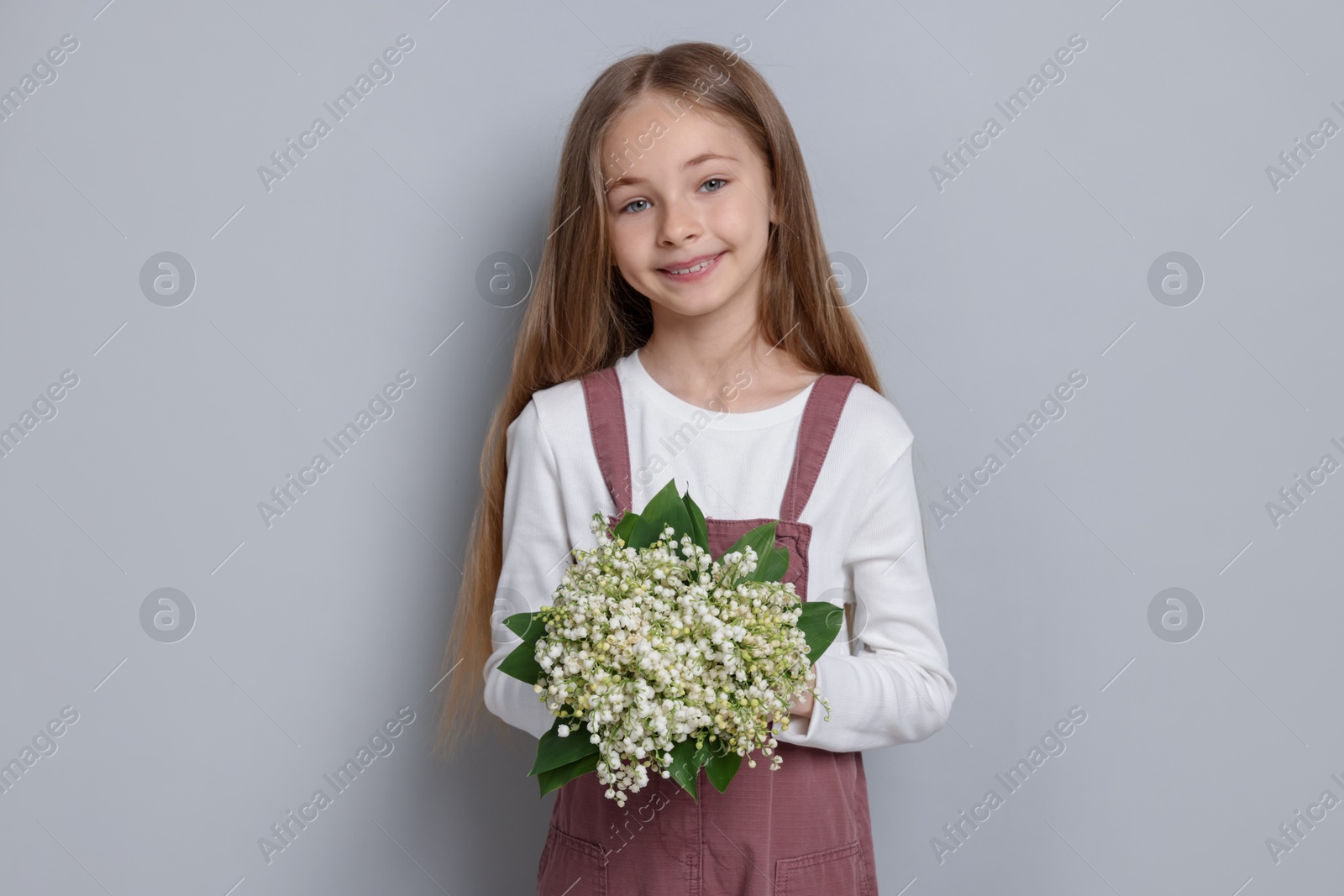 Girl with bouquet of beautiful lily-of-the-valley flowers on light grey background Photo of Girl with bouquet of beautiful lily-of-the-valley flowers on light grey background