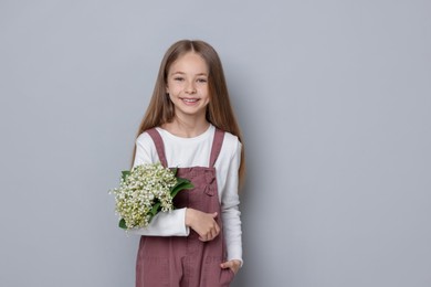 Photo of Girl with bouquet of beautiful lily-of-the-valley flowers on light grey background