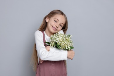 Photo of Girl with bouquet of beautiful lily-of-the-valley flowers on light grey background
