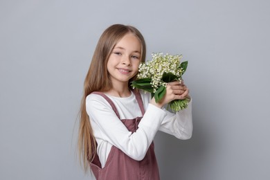 Photo of Girl with bouquet of beautiful lily-of-the-valley flowers on light grey background