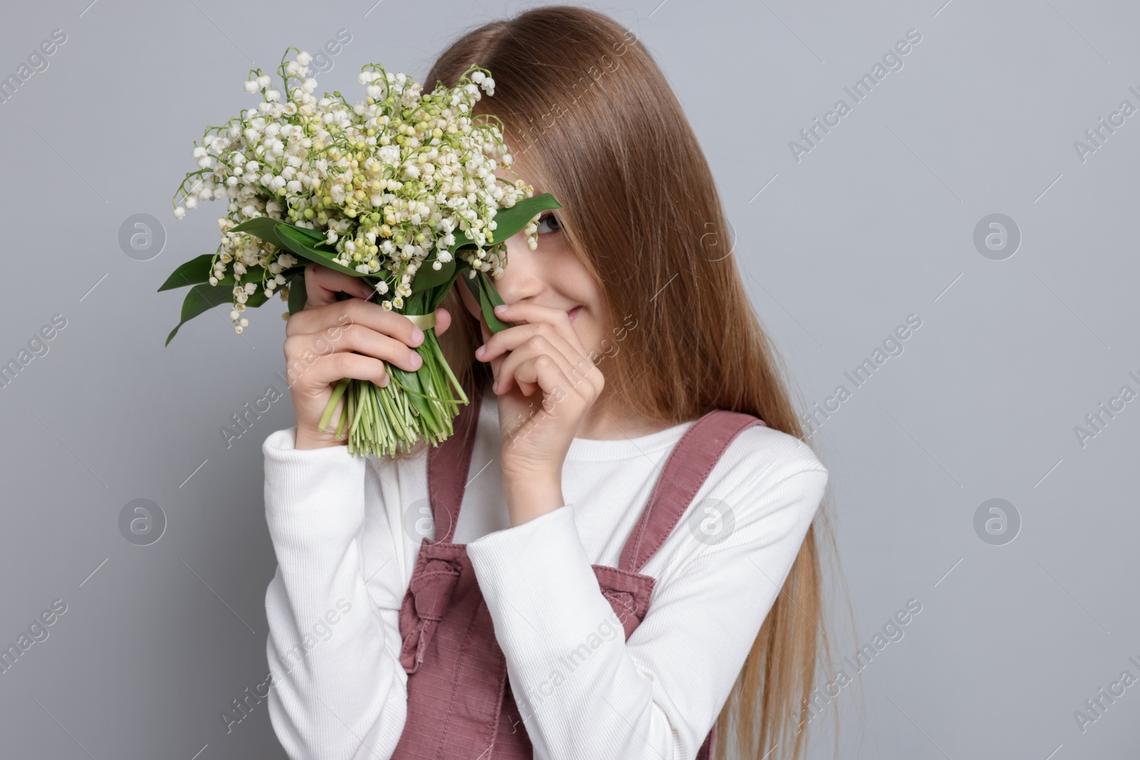 Girl with bouquet of beautiful lily-of-the-valley flowers on light grey background Photo of Girl with bouquet of beautiful lily-of-the-valley flowers on light grey background