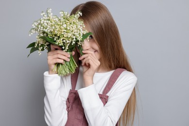 Photo of Girl with bouquet of beautiful lily-of-the-valley flowers on light grey background
