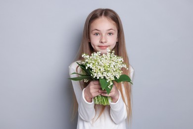 Photo of Girl with bouquet of beautiful lily-of-the-valley flowers on light grey background
