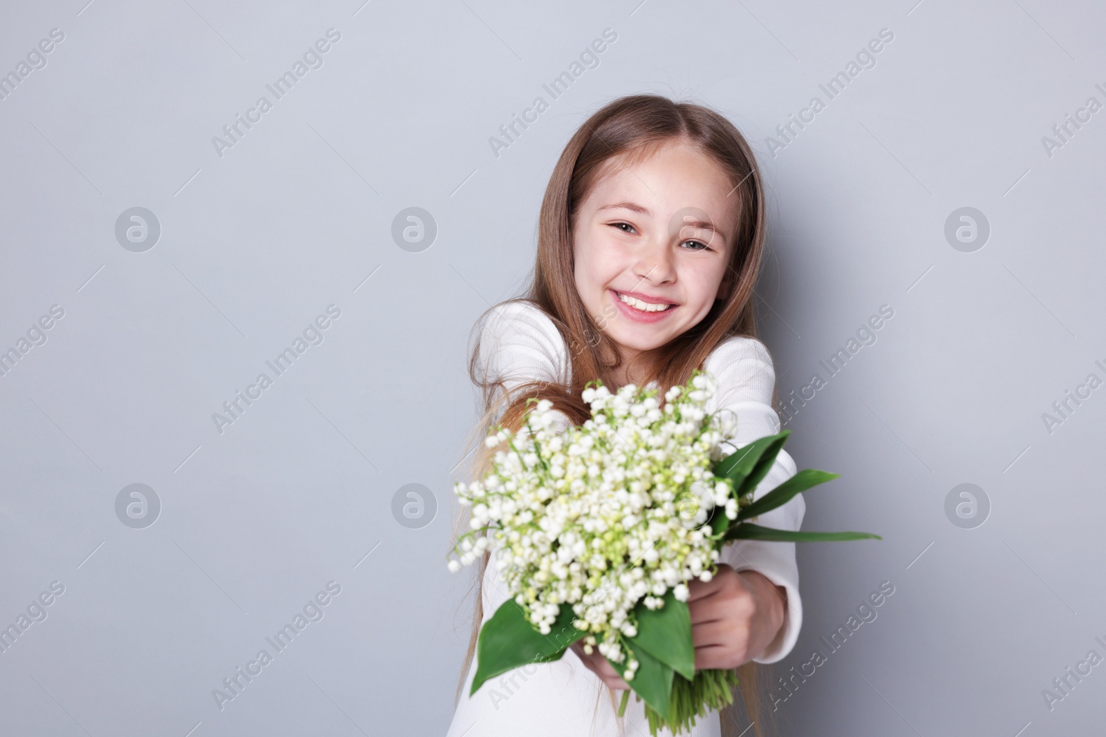 Girl with bouquet of beautiful lily-of-the-valley flowers on light grey background. Space for text Photo of Girl with bouquet of beautiful lily-of-the-valley flowers on light grey background. Space for text