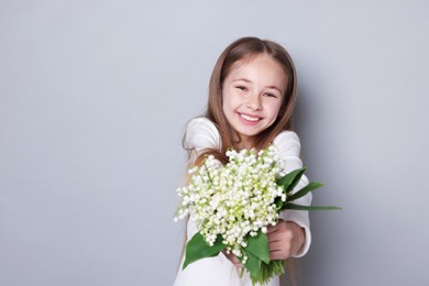 Photo of Girl with bouquet of beautiful lily-of-the-valley flowers on light grey background. Space for text