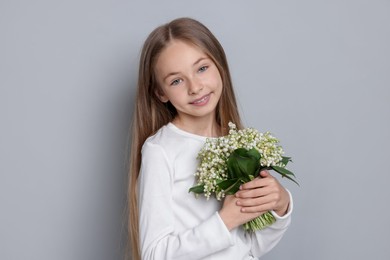 Photo of Girl with bouquet of beautiful lily-of-the-valley flowers on light grey background