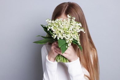Photo of Girl with bouquet of beautiful lily-of-the-valley flowers on light grey background