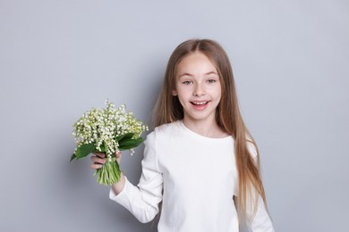 Photo of Girl with bouquet of beautiful lily-of-the-valley flowers on light grey background