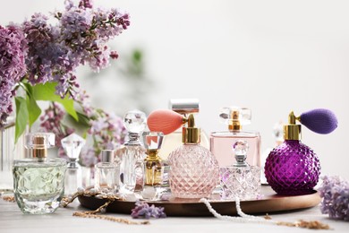 Photo of Bottles of perfumes, accessories and lilac flowers on white wooden table