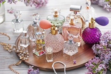 Photo of Bottles of perfumes, accessories and lilac flowers on white wooden table