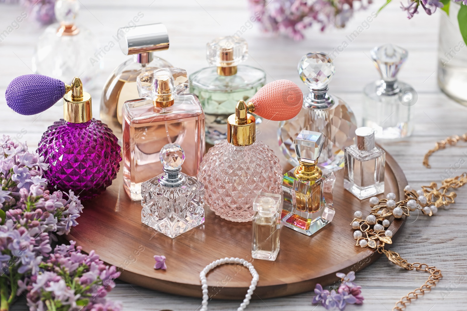 Photo of Bottles of perfumes, accessories and lilac flowers on white wooden table