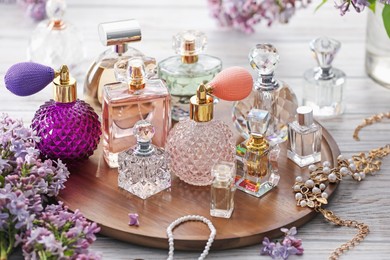 Photo of Bottles of perfumes, accessories and lilac flowers on white wooden table