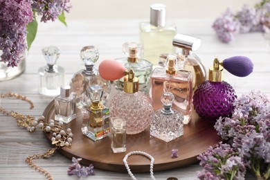 Photo of Bottles of perfumes, accessories and lilac flowers on white wooden table