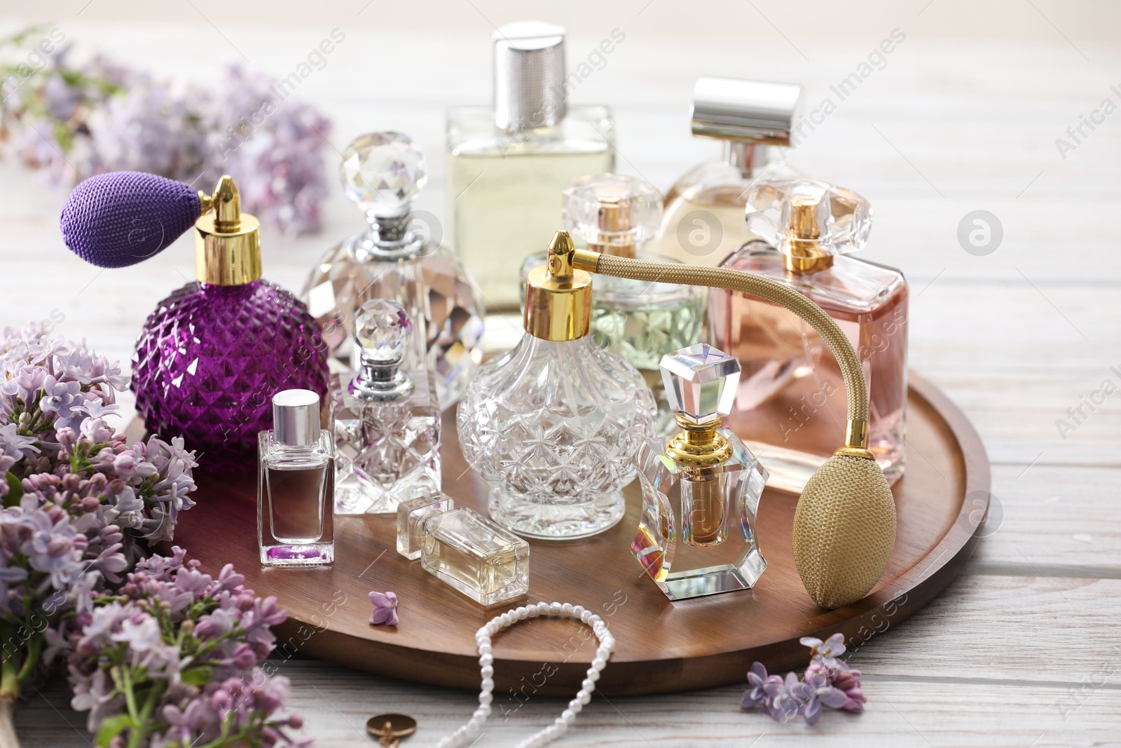 Bottles of perfumes, accessories and lilac flowers on white wooden table Photo of Bottles of perfumes, accessories and lilac flowers on white wooden table