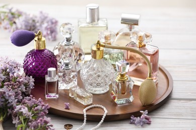 Photo of Bottles of perfumes, accessories and lilac flowers on white wooden table