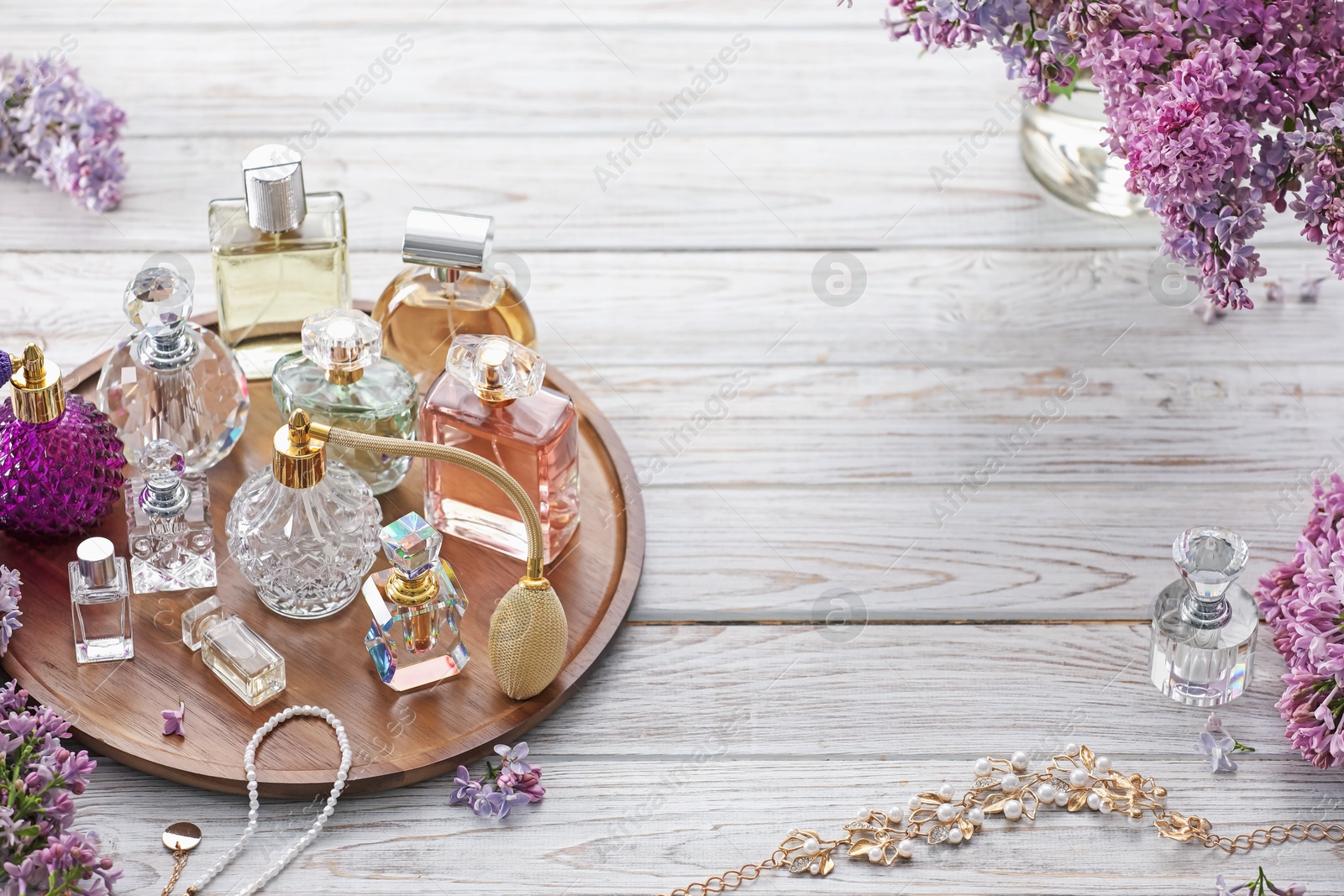 Bottles of perfumes, accessories and lilac flowers on white wooden table. Space for text Photo of Bottles of perfumes, accessories and lilac flowers on white wooden table. Space for text