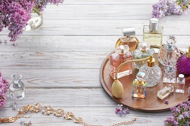 Photo of Bottles of perfumes, accessories and lilac flowers on white wooden table. Space for text