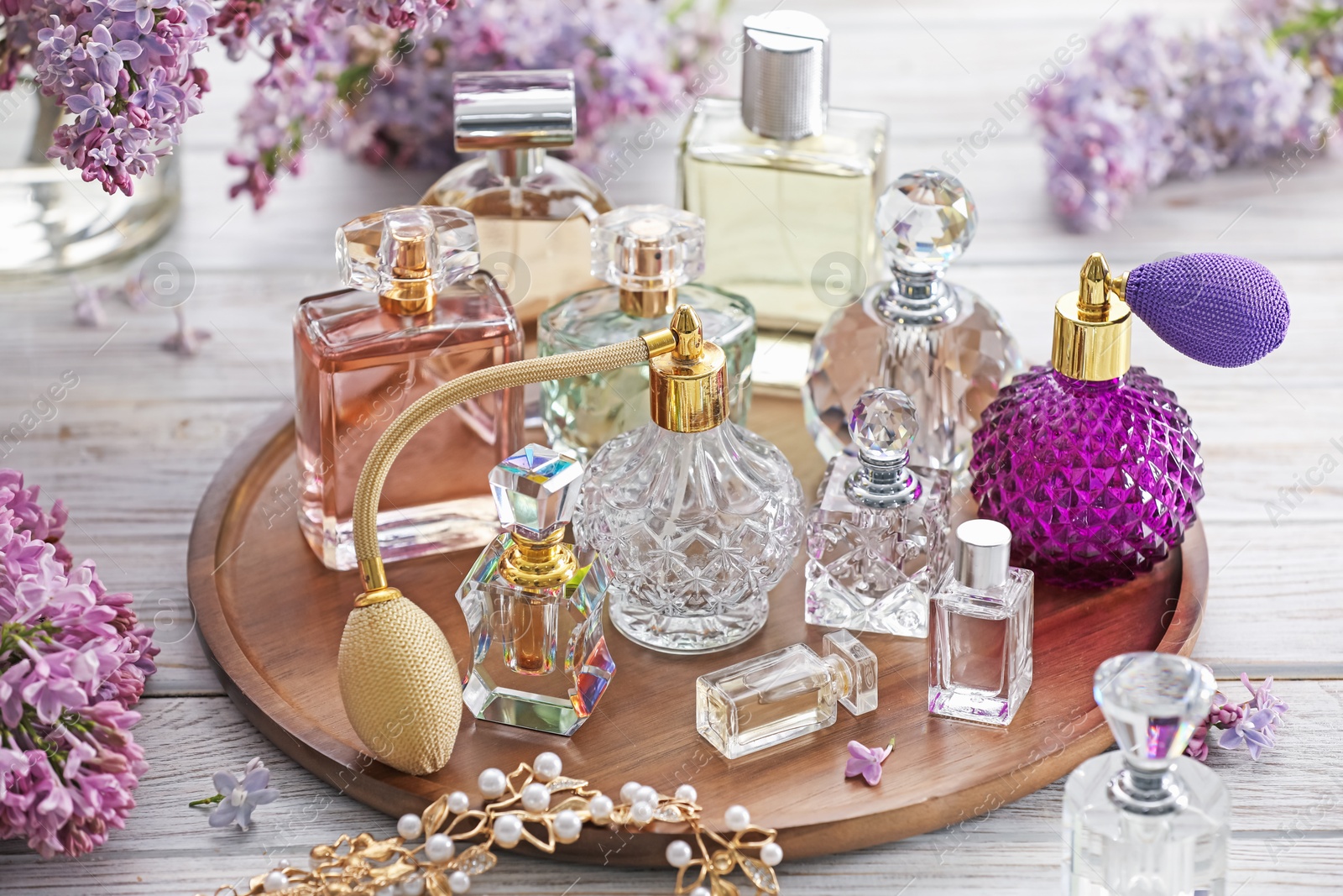 Bottles of perfumes, accessories and lilac flowers on white wooden table Photo of Bottles of perfumes, accessories and lilac flowers on white wooden table